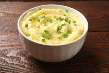 Tasty mashed potato with green onion in bowl on wooden table, closeup