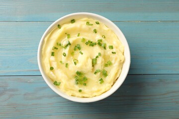 Tasty mashed potato with green onion in bowl on light blue wooden table, top view