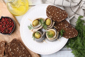 Delicious herring rolls with olives served on white wooden table, flat lay