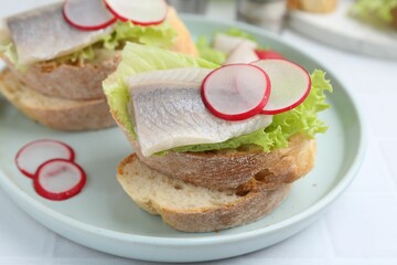 Tasty sandwiches with herring, radish and lettuce on white table, closeup