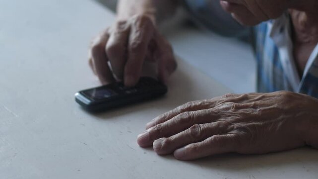 Hands of elderly man using vintage button mobile phone while sitting at table, pensioner making phone call with retro keypad device
