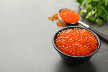 Tasty red caviar in bowl, spoon and parsley on grey table, closeup. Space for text