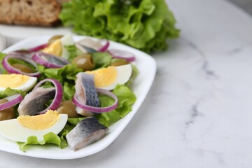 Delicious salad with herring, egg and vegetables on white marble table, closeup. Space for text