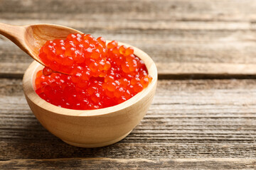 Taking red caviar with spoon from bowl at wooden table, closeup. Space for text