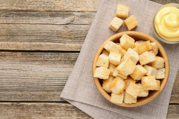Tasty crispy croutons in bowl and sauce on wooden table, top view. Space for text