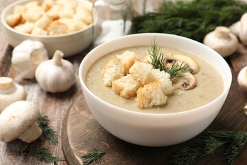 Delicious mushroom cream soup with croutons, dill and ingredients on wooden table, closeup