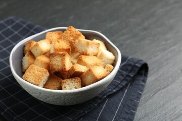 Tasty crispy croutons in bowl on dark textured table, closeup. Space for text