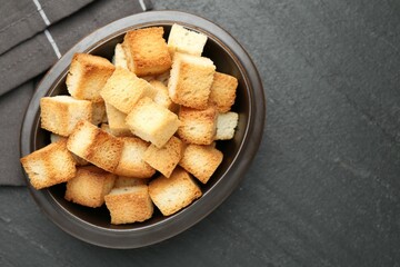 Tasty crispy croutons in bowl on dark textured table, top view. Space for text