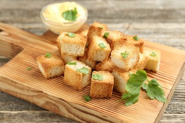 Tasty crispy croutons with cut parsley and sauce on wooden table, closeup
