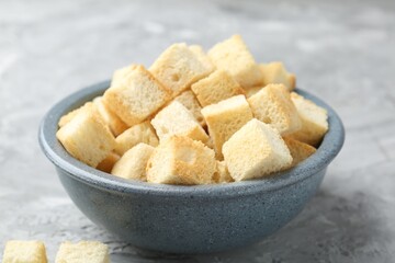 Tasty crispy croutons in bowl on grey textured table, closeup