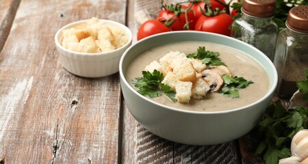Delicious mushroom cream soup with croutons, parsley and ingredients on wooden table, closeup