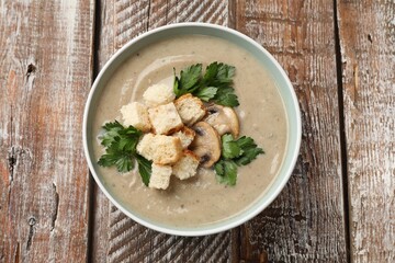 Delicious mushroom cream soup with croutons and parsley on wooden table, top view