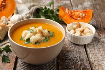 Tasty pumpkin cream soup with croutons and parsley in bowl on wooden table, closeup