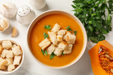Tasty pumpkin cream soup with croutons and parsley in bowl on white table, flat lay