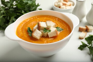 Tasty pumpkin cream soup with croutons and parsley in bowl on white table, closeup