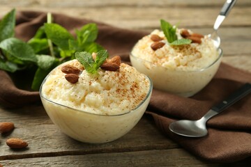 Delicious rice pudding with cinnamon, almonds and mint served on wooden table, closeup