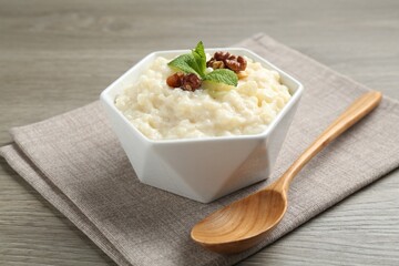 Delicious rice pudding with walnuts, mint and spoon on wooden table, closeup