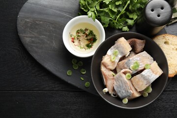 Pieces of delicious herring with green onions on black wooden table, flat lay. Space for text