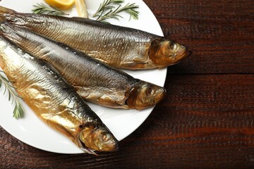 Smoked herrings, rosemary and lemon on wooden table, top view. Space for text