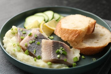 Pieces of delicious herring, mashed potato, cucumber slices and bread on black table, closeup