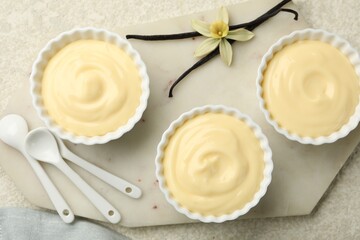 Tasty vanilla pudding with spoons, pods and flower on light textured table, flat lay