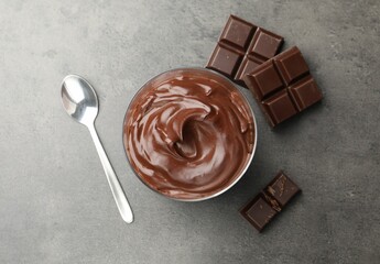 Tasty pudding and pieces of chocolate on grey table, flat lay