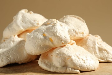 Delicious homemade meringue cookies on wooden table against beige background, closeup
