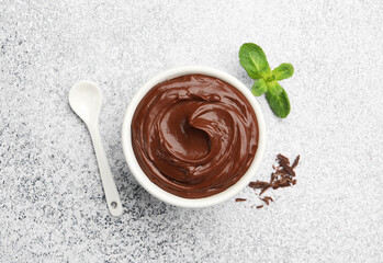 Delicious chocolate pudding in bowl, shavings, mint and spoon on light grey textured table, flat lay