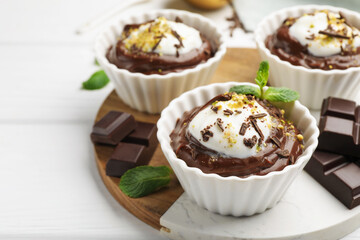 Tasty pudding with whipped cream in bowls and pieces of chocolate on white wooden table, closeup