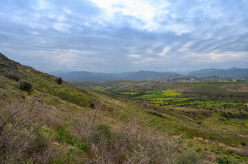Exploring the serene hill landscapes with sprawling green fields and distant mountains under a cloudy sky