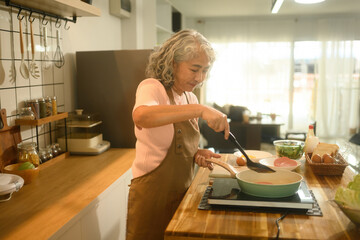 An elderly woman wearing an apron cooking breakfast in a kitchen, Focused on frying ham, with fresh ingredients ready for a homemade meal