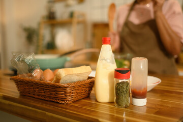 Close-up view of cooking ingredients including bread, eggs, mayonnaise, spices, and sauces on a wooden kitchen counter, ready for a homemade meal.