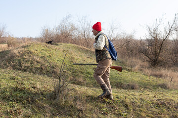 Mature hunter man holding a shotgun and walking through a field