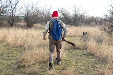Mature hunter man holding a shotgun and walking through a field