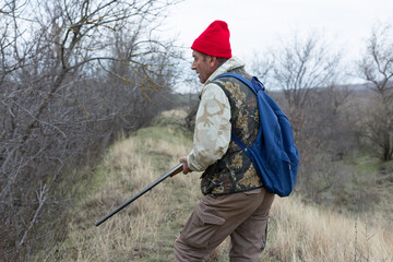 Mature hunter man holding a shotgun and walking through a field