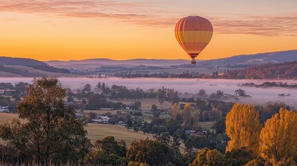 Hot air balloon floats over misty valley at sunrise.