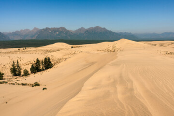 Desert surrounded by forest and mountains. Chara sands and Kodar mountain range. Summer natural unusual landscape.