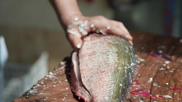 A close-up of a man's hands cleaning the internal organs of a fish and cutting