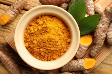 Turmeric powder in bowl, roots and leaves on wooden table, flat lay