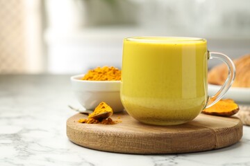 Delicious turmeric latte, powder and rhizomes on white marble table, closeup