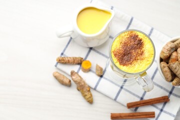 Delicious turmeric latte and rhizomes on white wooden table, flat lay. Space for text