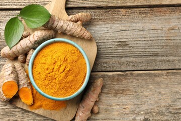 Turmeric powder in bowl, roots and leaves on wooden table, flat lay. Space for text