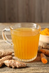 Aromatic turmeric tea in glass mug, roots and powder on wooden table, closeup