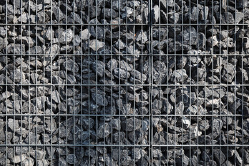 A tightly packed gabion wall consisting of rough gray rocks held together in a structured metal...