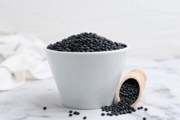 Black lentils on white marble table, closeup