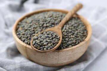 Green lentils in bowl and spoon on light table, closeup
