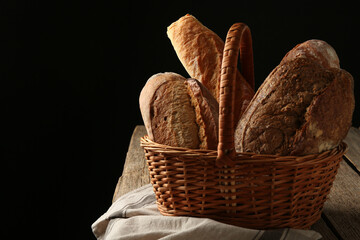 Different loaves of fresh bread in basket on wooden table, closeup. Space for text