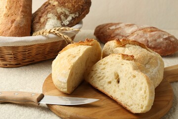 Different types of fresh bread, knife and spikelets on light textured table, closeup