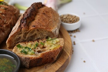 Tasty bread with garlic, herbs and oil on white tiled table, closeup. Space for text