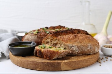 Tasty bread with garlic, herbs and oil on white tiled table, closeup